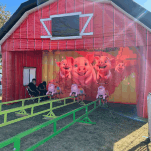 Bright red barn-themed inflatable with pig characters for fun pig races at parties and festivals.