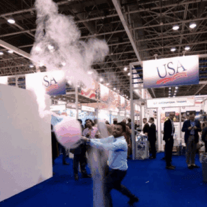 Man creating cotton candy at an indoor event with USA signage in background.
