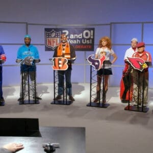 Group of people at a game show podium with NFL-themed props in a studio setting.