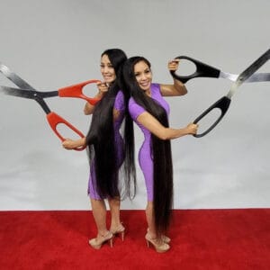 Two women holding oversized scissors for a grand opening celebration.