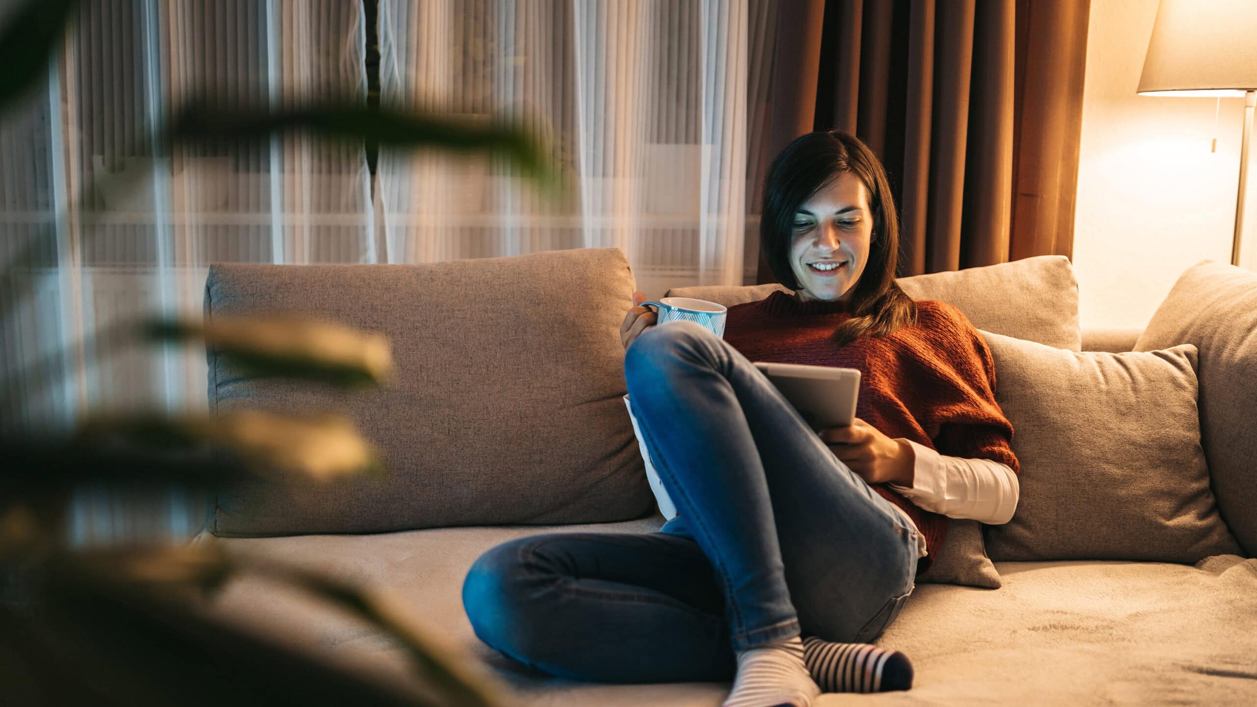Kvinna sitter i en soffa och surfar på internet med en surfplatta.