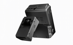 Compact black electronic device on a metal mounting bracket with ventilation slits, likely a projector or camera accessory viewed from an angled side.
