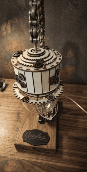 Lampe de bureau artisanale style Steampunk créée par Gravlaz, avec un bras en chaîne de moto recyclée, un abat-jour en bois gravé au laser avec engrenages et une ampoule vintage à filament Edison, posée sur un socle en bois massif