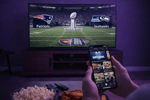 Super Bowl TikTok Trends: A person holding a smartphone showing the TikTok app in front of a television broadcasting a 2026 Super Bowl game between the Patriots and Seahawks.
