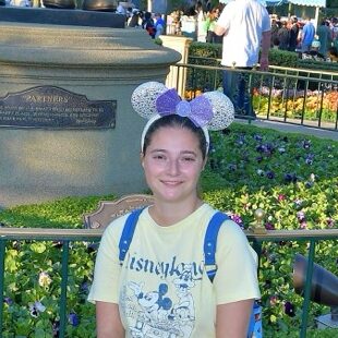 Vibrant Disney theme park visitor with Mickey Mouse ears in front of floral garden MIDs.