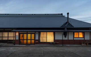 Traditional Japanese kominka farmhouse exterior at dusk with warm interior lighting