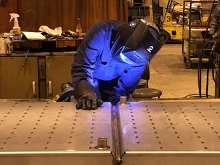 Welding operator welding the underside of a flat piece of metal