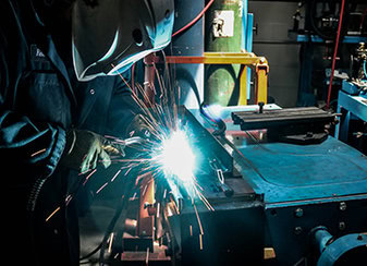 Welder bent over MIG welding part on table