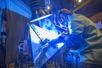 Side view of a welder welding on a rotating part with a fume extraction arm above