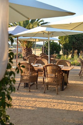Elegant outdoor dining area with wicker chairs and large parasols, perfect for enjoying meals in a relaxing garden setting at Can Camades.