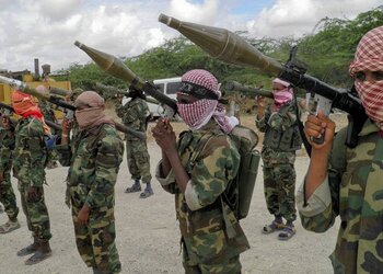 Line of masked soldiers in camouflage uniforms aiming shoulder-fired weapons with large rocket launchers in a dusty outdoor area.