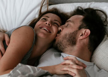 A joyful couple cuddling and smiling in bed, showcasing intimacy and emotional connection.