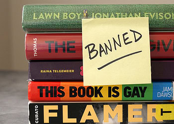 Books with sticky note labeled "BANNED" placed over titles, highlighting censorship of literary works in the context of psychological and societal impacts.