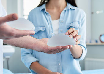 Silicone breast implants being examined by a healthcare professional in a clinical setting.