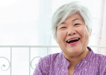 Joyful elderly woman with gray hair laughing, bright background, expressing happiness and positive emotions in a home setting.