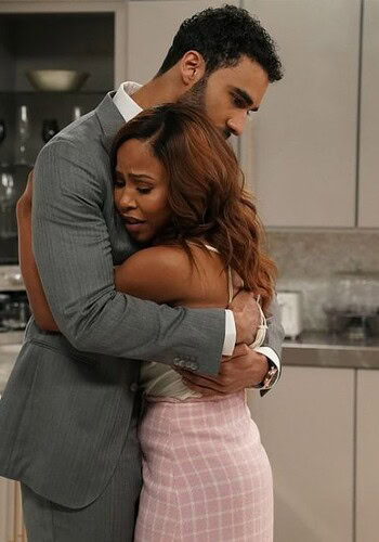 Andi Barnes, dressed in a pink skirt, embraces Robin in a tender moment in a kitchen setting from Tyler Perry's Sistas.