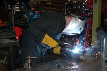 Image of welder leaning over to see the weld contact tip more closely