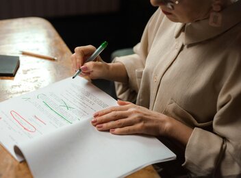pexels-photo-7968063-7968063 Close-up of a senior woman editing a manuscript at a desk with a green marker indoors.