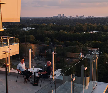 Two coworkers share a cocktail at a bistro table on the balcony of a modern Raleigh office space