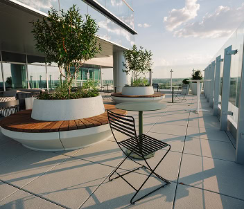 A bistro chair overlooks beautifully landscaped greenspace on the balcony of a modern Raleigh office tower
