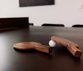 Solid wood ping pong paddles rest next to a white ball on a dark oak table in the rec room of an amenity-rich luxury Raleigh apartment