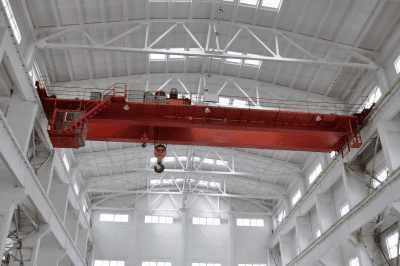 Top-running red overhead bridge crane with hoist inside a bright industrial bay, illustrating overhead crane maintenance and inspection.
