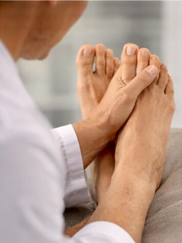 A person in a white shirt massages another person's bare foot, focusing on the toes, in a bright indoor setting.