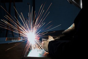 Closeup of welding operator holding MIG gun with sparks flying