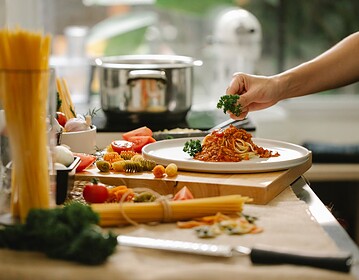 Crop anonymous chef adding parsley to spaghetti with tomato and meat while cooking lunch in kitchen