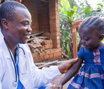 Health worker engaging with young girl in rural African setting.