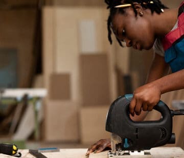 Young woman operating a jigsaw saw in a woodworking workshop.