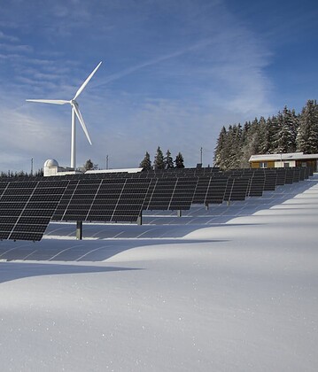 Solar panels and wind turbine in a snowy landscape, showcasing renewable energy sources.