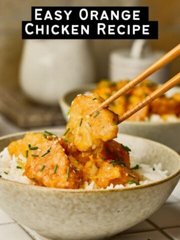 Vertical shot of chopsticks grabbing a piece of glossy orange chicken from a bowl of rice.