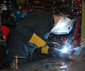 Image of a welder bending over a table welding.