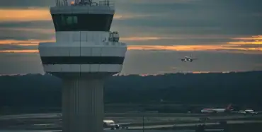 Airport air traffic control tower at sunset with aircraft on final approach