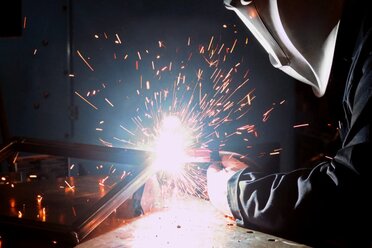 Side view of welder welding a square part on a table