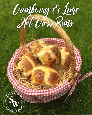 Cranberry and Lime Hot Cross Buns on a checked cloth in a wicker basket