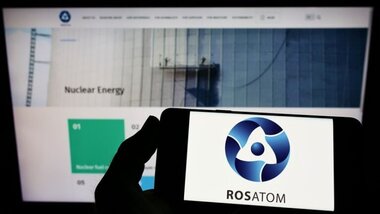 smartfon, na ekranie napis Rosatom, w tle blok elektrowni atomowej