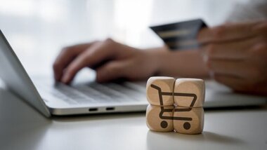 człowiek z kartą w dłoni, laptop, klocki z symbolem e-commerce