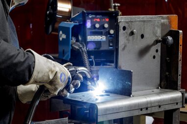 Close up of welder's hand holding a MIG gun to weld on part