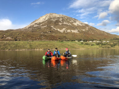 Smiling group kayaking at sunset in Dunlewey Lake