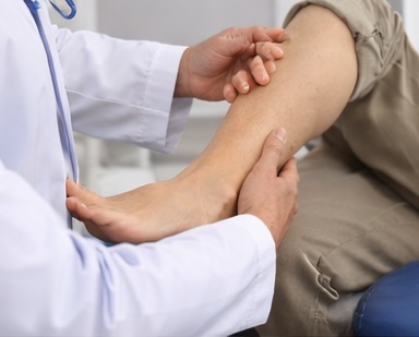 A doctor examines a patient's ankle and foot while the patient is seated, focusing on the lower leg and ankle area.