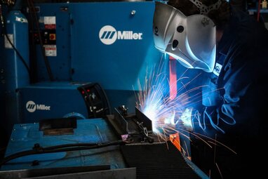 Side view of a welding operator MIG welding with Miller machines in the background