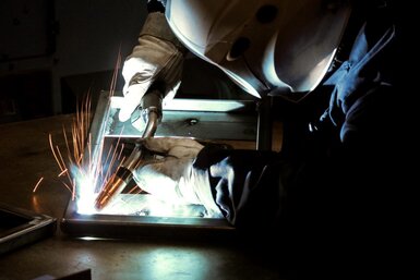 Side view of welder welding on square part with sparks