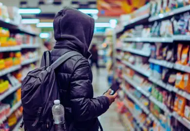 person standing in store aisle with coat on and hood up, symbolizing potential shoplifting