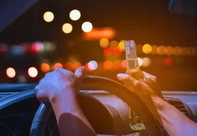 Guy holding a bottle of beer while driving.