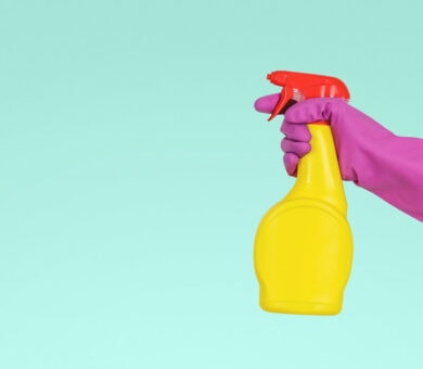 Eine Hand, die einen Gummihandschuh trägt, hält eine Sprühflasche