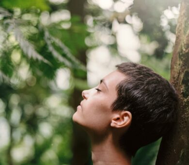 Frau lehnt an einem Baum im Wald und atmet