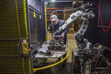 Image of a robotic operator with a teach pendant by a robotic MIG welding cell