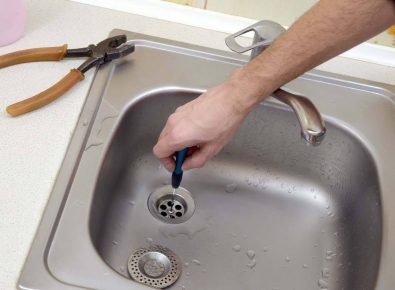 Hand holding a kitchen sink basket strainer in place while repairing a leak
